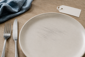 Matte ceramic dinner plate with subtle gray cutlery marks, stainless steel fork, knife, cloth, and blank sample tag