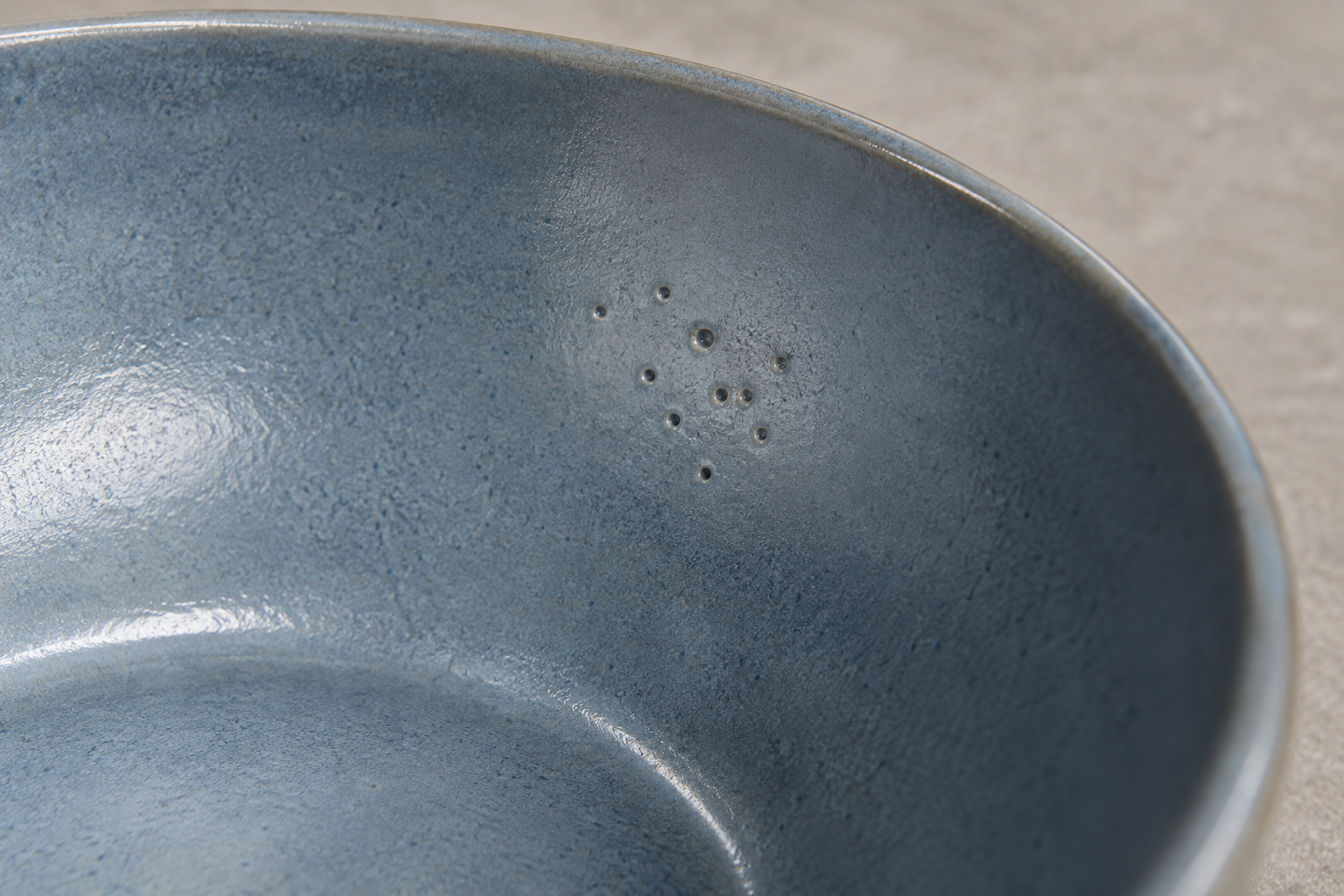 Close view of small pinholes in a blue-gray ceramic bowl glaze, showing a surface issue that can hold a batch