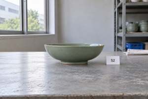 Side view of a shallow green ceramic bowl beside a sample card marked S2, showing its rim, curved wall and foot ring