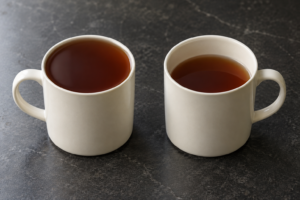 Two matching cream ceramic mugs with dark liquid at different fill levels, showing brimful and usable capacity