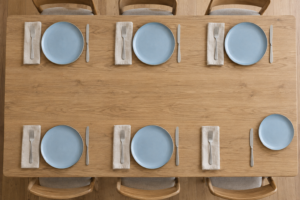 Overhead view of six simple table settings with one replacement ceramic dinner plate beside an empty setting