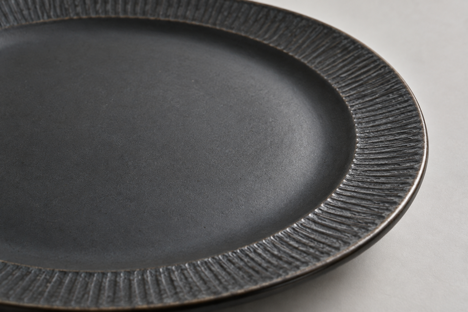 Close detail of a charcoal ceramic plate with a smooth glazed center and a textured outer rim under soft side light