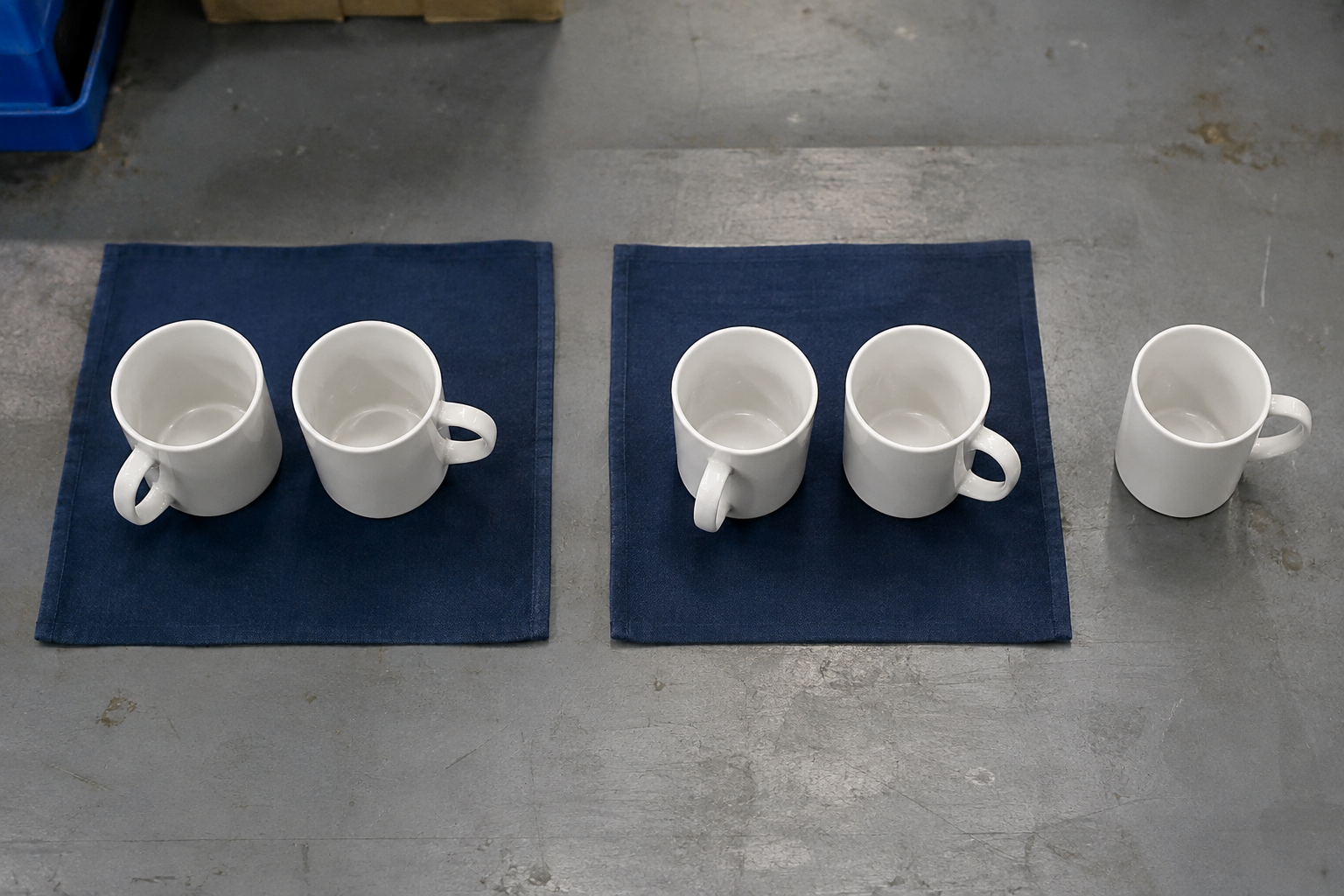 Overhead view of two paired ceramic mug sets and one separate spare mug on a warehouse sorting mat before packing