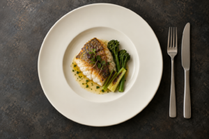 Overhead view of a cream ceramic plate with a small fish course, sauce and garnish inside a clear carrying rim