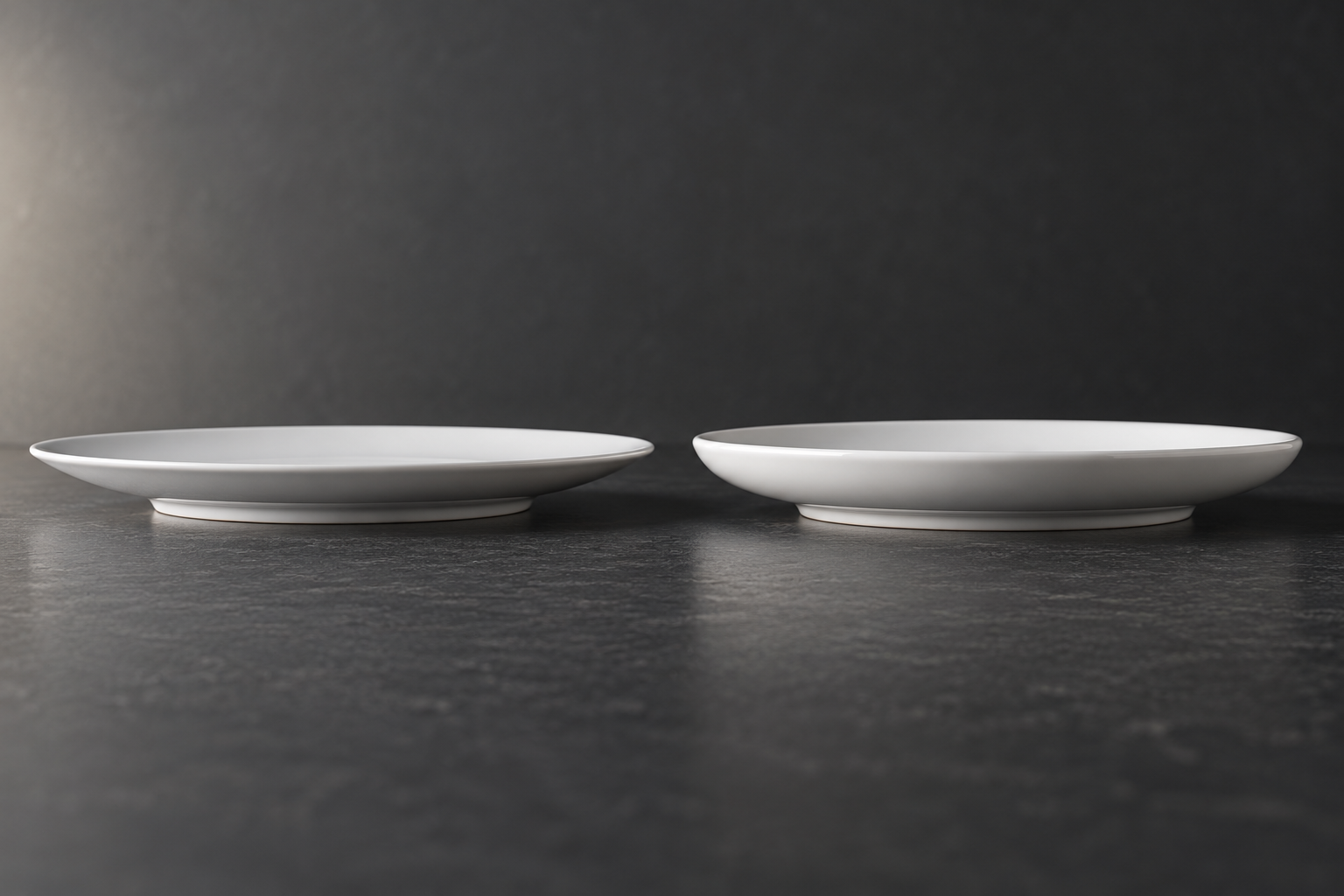 Low side view of two white porcelain plates showing different rim profiles and foot rings on a dark comparison surface